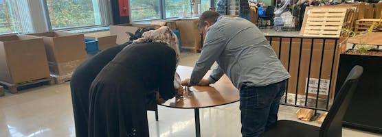 3 mensnen staan over tafel gebogen om opdracht te maken