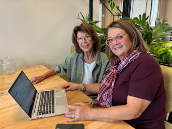 Twee vrouwen met laptop aan tafel, omringd door planten