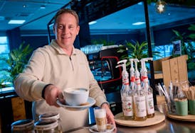 Man serveert koffie met siropen op de achtergrond.