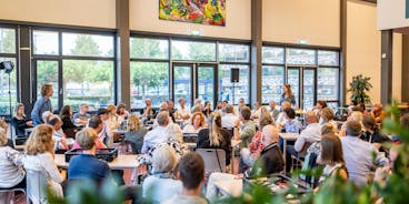 Mensen in een grote zaal tijdens een bijeenkomst.