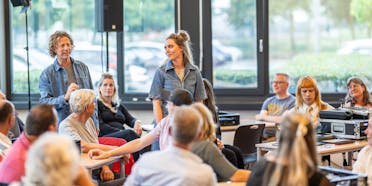 Twee presentatoren spreken voor een publiek.