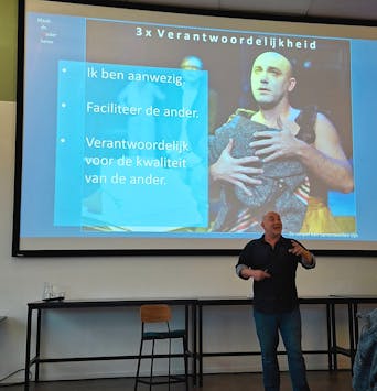Man spreekt voor publiek, presentatie op de achtergrond.