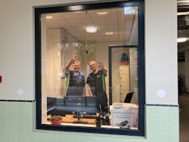 Twee mensen zwaaien vanuit een kantoorraam.