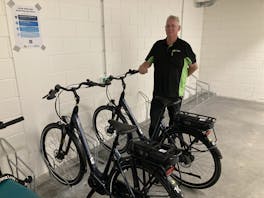 Man staat naast twee elektrische fietsen in fietsenstalling.