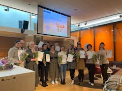 Groep mensen met bloemen en diploma's in een zaal.