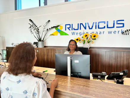 vrouw staat bij receptioniste aan de balie