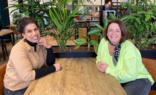 Twee vrouwen zitten aan een houten tafel met planten.