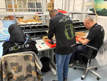 Drie mensen werken aan een bureau met dozen.