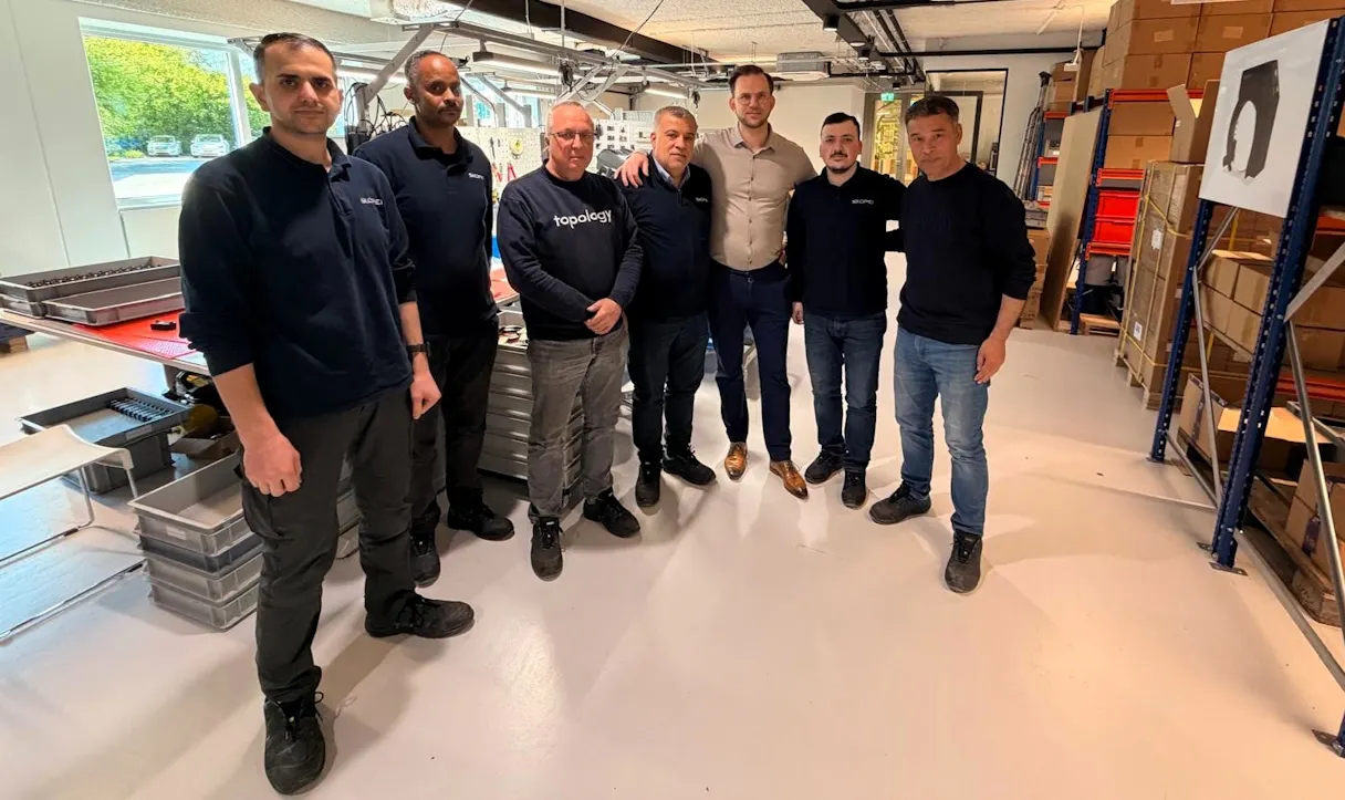 Groep mannen in een fabriek, glimlachend samen.