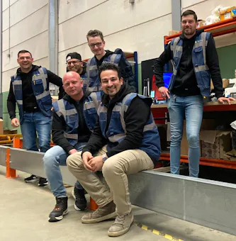 Zes medewerkers poseren in een magazijn.