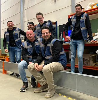 Zes medewerkers poseren in een magazijn.