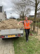 Man in veiligheidshesje leunt op een aanhanger met stro.