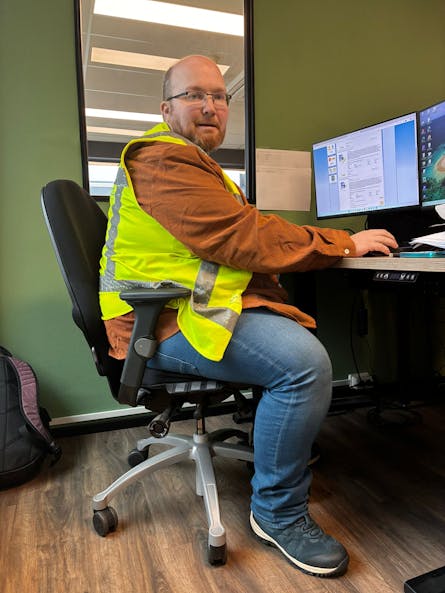 Man met veiligheidsvest achter bureau in kantoor.