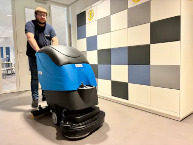 Man met een schrobmachine in een kantooromgeving.