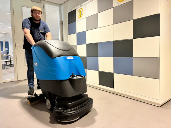 Een man bedient een blauwe schoonmaakmachine.