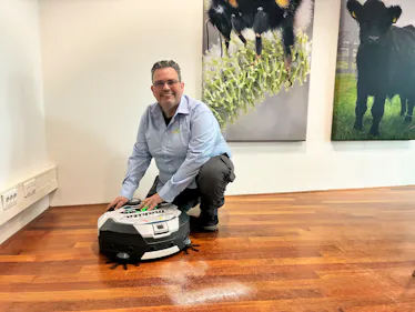 Man knielt naast een robotstofzuiger op houten vloer.