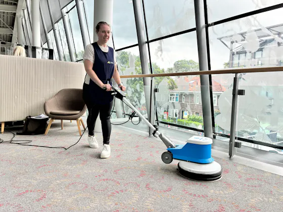 Vrouw die vloer aan het schrobben is met een machine.