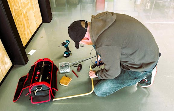 Man met gereedschap aan het werk op vloer.