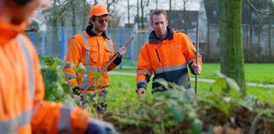 Twee mannen in oranje werkkleding werken buiten.