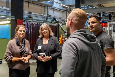 Vier mensen praten in een industriële werkplaats.
