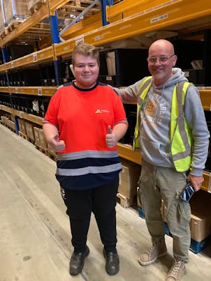 Twee mannen in een magazijn, beide geven duimen omhoog.