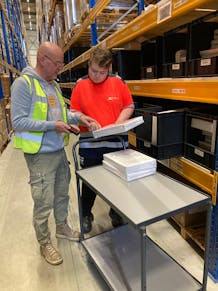 Twee mensen bespreken documenten in een magazijn.