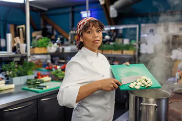 Vrouwelijke chef-kok snijdt groenten in een keuken.